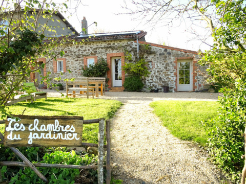 Photo d’une maison en pierre rustique, jardin verdoyant et panneau ‘Les chambres du jardinier’ devant.