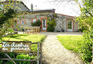 Photo d’une maison en pierre rustique, jardin verdoyant et panneau ‘Les chambres du jardinier’ devant.