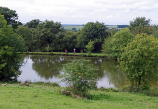 Ein ruhiger Teich mit Bäumen an der Feather Down La Flocellière en Vendée Ferienpark in Pays de la Loire, Frankreich.