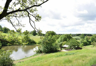 Udsigt over en grøn bakke, sø og træer ved Feather Down La Flocellière en Vendée, feriepark i Pays de la Loire.