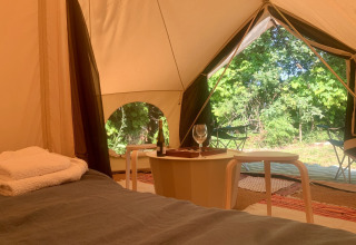 Vista interior de la tienda Camelia XL Bell Tent en Glamping de Cerveira, Portugal, con cama y mesa.