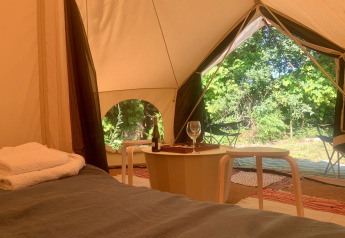 Vista interior de la tienda Camelia XL Bell Tent en Glamping de Cerveira, Portugal, con cama y mesa.