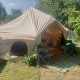 Camelia XL Bell Tent safari telt med åbning, to stole og grøn måtte udenfor, omgivet af træer og planter.