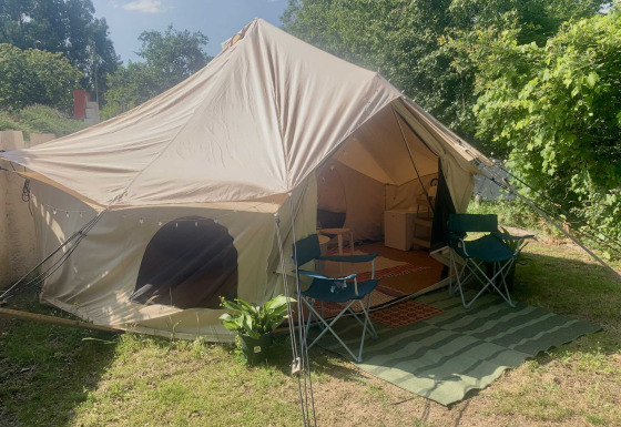 Camelia XL Bell Tent safaritent met geopende ingang, twee stoelen en een buitentapijt tussen het groen.