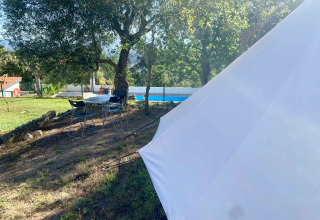 Area glamping al Glamping de Cerveira nel nord del Portogallo con tenda, sedie, tavolo e piscina.