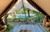 Udsigt fra en safaritelts indgang mod en pool og have hos Glamping de Cerveira, Portugal.