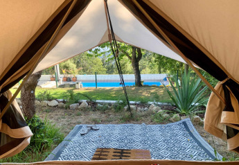 Udsigt fra en safaritelts indgang mod en pool og have hos Glamping de Cerveira, Portugal.