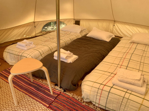 Tres camas individuales y una mesa pequeña en la tienda Oliveira Bell de Glamping de Cerveira, Portugal.