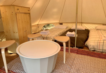 Indretning af Oliveira Bell Standard Bell Tent med tre senge, træmøbler og tæpper hos Glamping de Cerveira.