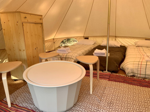 Indretning af Oliveira Bell Standard Bell Tent med tre senge, træmøbler og tæpper hos Glamping de Cerveira.