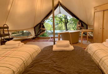 Interior de la tienda Oliveira Bell Standard en Glamping de Cerveira, Portugal, con dos camas y bañera.