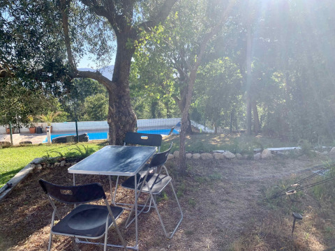 Mesa y sillas al aire libre bajo árboles junto a la piscina en Glamping de Cerveira, norte de Portugal.