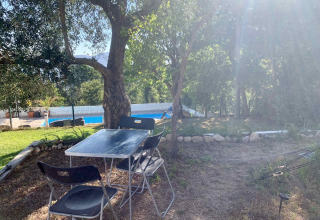 Udendørs bord og stole under træer ved pool på Glamping de Cerveira, feriepark i det nordlige Portugal.