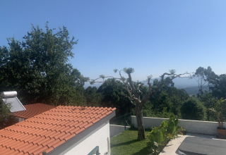 Udsigt over Glamping de Cerveira med rødt tegltag, træer og udsigt til frodige bakker i Portugal.