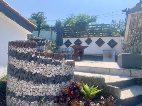 Espace extérieur de Glamping de Cerveira, Portugal, avec mur gabion, plantes grasses et terrasse ensoleillée.