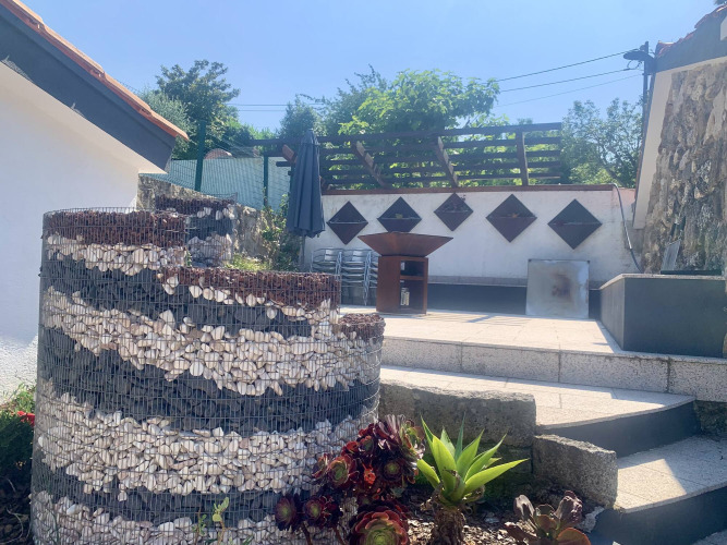 Espace extérieur de Glamping de Cerveira, Portugal, avec mur gabion, plantes grasses et terrasse ensoleillée.