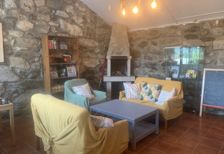 Hyggelig opholdsstue med stenvægge, pejs, farverige sofaer og bogreol i Glamping de Cerveira, Portugal.