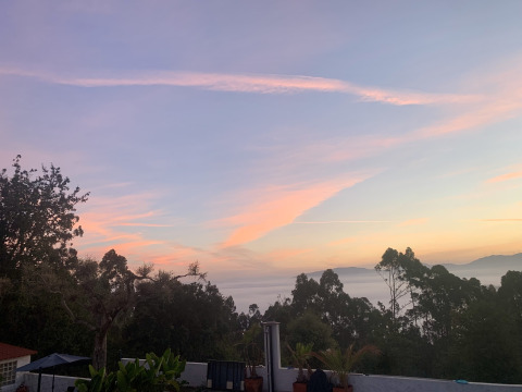 Vista dal Glamping de Cerveira nel nord del Portogallo al tramonto con alberi, terrazza e cielo colorato.