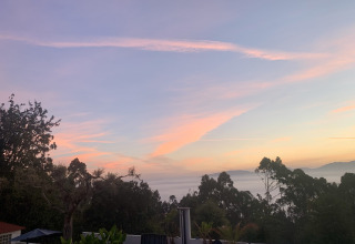 Udsigt over Glamping de Cerveira i Nordportugal ved solnedgang med træer, terrasser og farverig himmel.