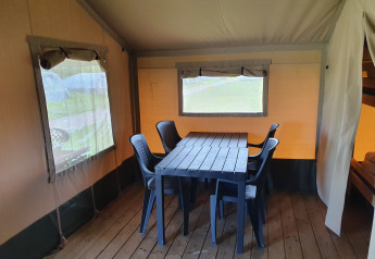 Interior de tienda safari en Camping de Oude Rijn, Países Bajos, con mesa, sillas, suelo de madera y ventanas.