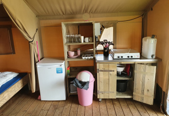 Cocina pequeña dentro de una tienda safari con nevera, estanterías abiertas y utensilios de cocina.