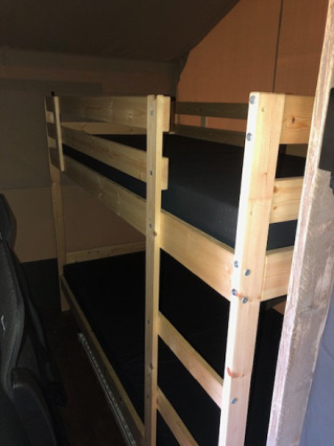 Interior view of a wooden bed frame in a safari tent with sanitary facilities at Camping Bockenauer Schweiz.