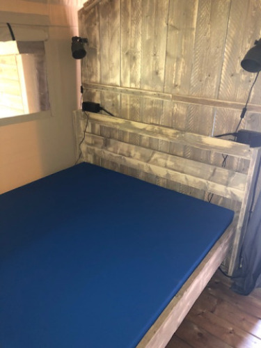 Interior of a safari tent with wood paneling, blue mattress, and spotlights at Camping Bockenauer Schweiz, Germany.