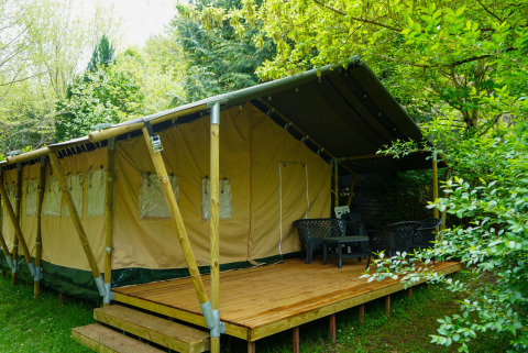 Safari-Zelt mit Holzterrasse und Gartenmöbeln, umgeben von üppigem Grün, perfekt zum Glamping.