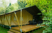 Safari-Zelt mit Holzterrasse und Gartenmöbeln, umgeben von üppigem Grün, perfekt zum Glamping.