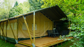 Safaritent met houten terras en comfortabele stoelen, omgeven door weelderig groen, ideaal voor glamping.