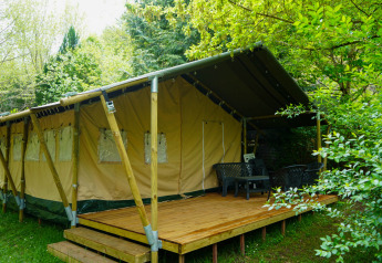 Tienda safari con terraza de madera y sillas al aire libre, rodeada de vegetación exuberante y natural.