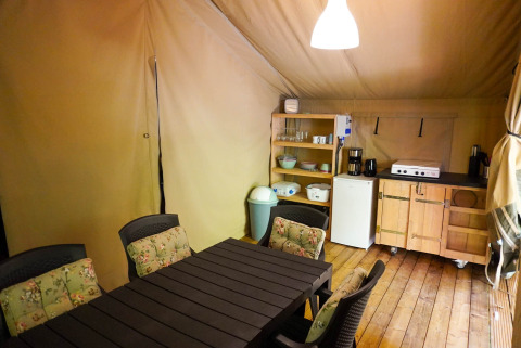Indretning af safaritelten Camping Pittoresque i Frankrig med spisebord, stole og simpelt køkken.