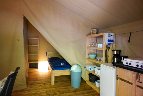 Interior view of a safari tent at Camping Pittoresque in France with bed, shelves, and kitchen area.