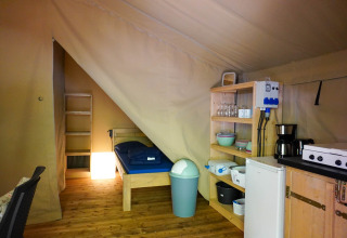 Interior view of a safari tent at Camping Pittoresque in France with bed, shelves, and kitchen area.
