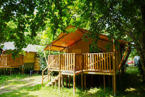 Safari tent at Camping Pittoresque in France, featuring a wooden deck shaded by lush green trees.