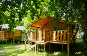 Safaritent op Camping Pittoresque in Frankrijk, met houten terras onder groene en schaduwrijke bomen.