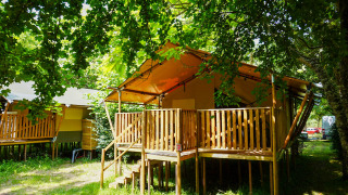 Safarizelt auf Camping Pittoresque in Frankreich, mit Holzterrasse unter grünen Bäumen im Sommerlicht.