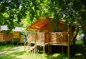 Safarizelt auf Camping Pittoresque in Frankreich, mit Holzterrasse unter grünen Bäumen im Sommerlicht.