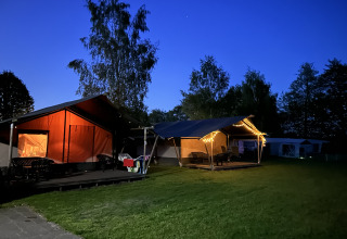 Vista nocturna de tienda safari con baño en Camping Emmen, Países Bajos, decorada con luces cálidas.