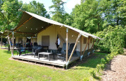 Safari telt på Camping Emmen i Holland, omgivet af grønne træer og med udendørs siddeområde.