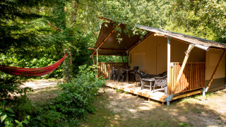 Tienda safari en Camping Fargogne, Francia, con porche, muebles de jardín y hamaca en entorno natural.