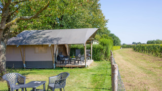 Tienda safari con terraza y asientos en Camping de Boomgaard, Bélgica, junto a campos verdes.