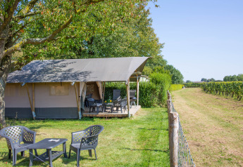 Tienda safari con terraza y asientos en Camping de Boomgaard, Bélgica, junto a campos verdes.
