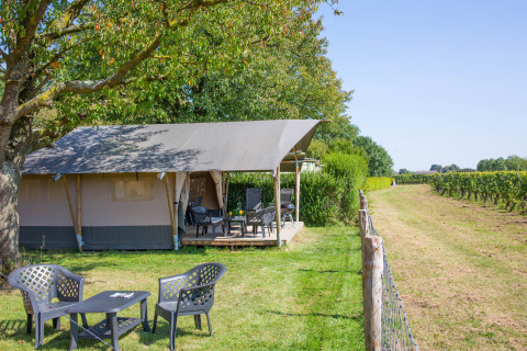 Safari tent with terrace and seating at Camping de Boomgaard in Belgium, overlooking green fields.