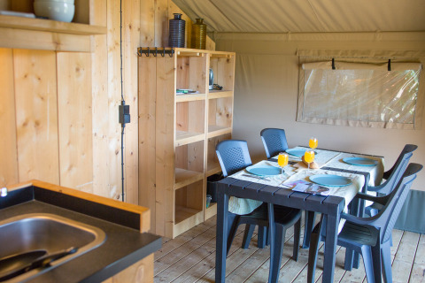 Indvendig udsigt af safari telt med spisebord, stole, træreoler og et lille køkken i Belgien.