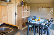 Interior de tienda safari en Camping de Boomgaard, Bélgica, con mesa, sillas, estanterías y fregadero.