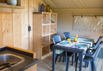 Interior of Safari tent at Camping de Boomgaard, Belgium, with dining table, chairs, shelves, and sink.