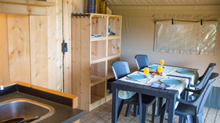 Innenansicht eines Safarizelts mit Esstisch, Stühlen, Holzmöbeln und Küche auf Camping de Boomgaard.