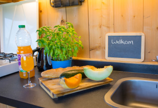 Encimera con pan, fruta, jugo y hierbas junto a un letrero de bienvenida en una tienda safari en Bélgica.