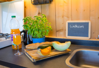 Piano cucina con pane, frutta, succo e erbe accanto a un cartello di benvenuto in una tenda safari in Belgio.